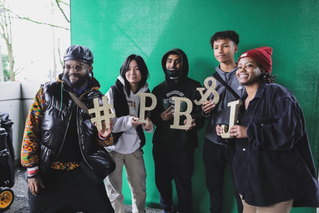 A photo of five happy people each of them is holding a glittery gold letter that together spells #PB&J