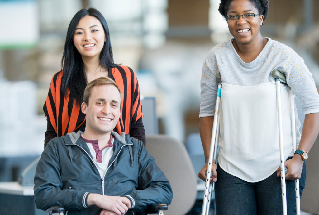 Three people pose for photo, with one on crutches and one in wheelchair